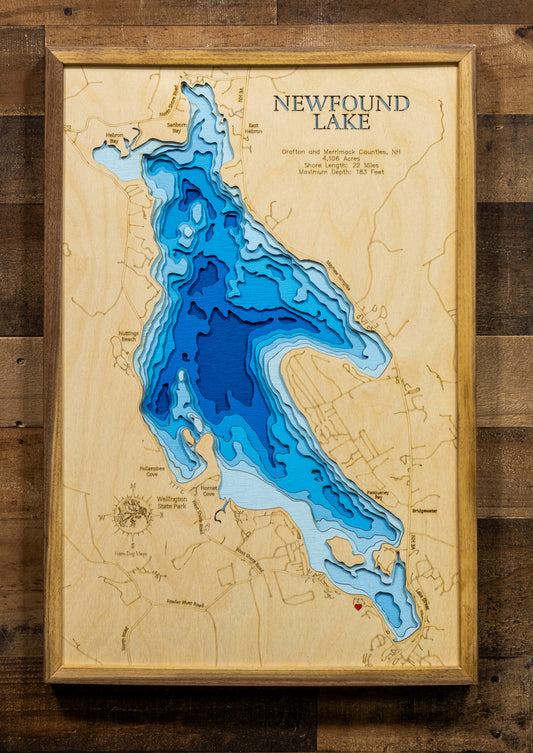 A laser-cut, layered wooden map of Newfound Lake, located in Grafton and Merrimack Counties, New Hampshire. The distinct shape of the lake is clearly visible within the central New Hampshire landscape. The varying depths of the lake, reaching an impressive maximum of 183 feet, are represented by different layers of wood, highlighting its significant depth and clarity.