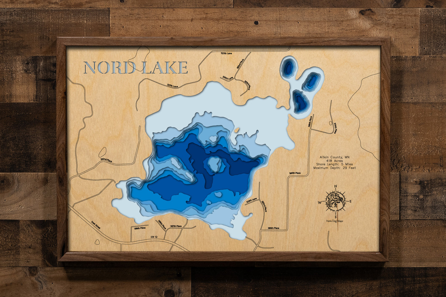 A detailed, laser-cut, multi-layered wooden map of Nord Lake in Aitkin County, Minnesota, showcasing the 418-acre lake with 5 miles of shoreline surrounded by forest and bog near Aitkin. The topographic design features natural wood layers highlighting the northern pike and bluegill fishery and graduated blue water layers illustrating depths to the 29-foot maximum.