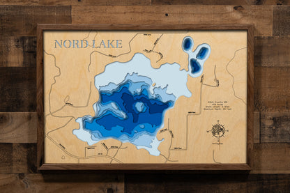 A detailed, laser-cut, multi-layered wooden map of Nord Lake in Aitkin County, Minnesota, showcasing the 418-acre lake with 5 miles of shoreline surrounded by forest and bog near Aitkin. The topographic design features natural wood layers highlighting the northern pike and bluegill fishery and graduated blue water layers illustrating depths to the 29-foot maximum.