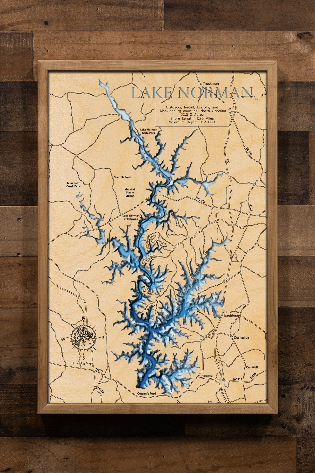 A laser-cut, layered wooden map of Lake Norman in North Carolina. The expansive and highly irregular shape of this large reservoir, with its numerous arms and 520-mile shoreline, is clearly visible as it winds through Iredell, Lincoln, Catawba, and Mecklenburg Counties. The varying depths of the lake, reaching a maximum of 110 feet, are represented by different layers of wood, illustrating its impressive underwater topography.