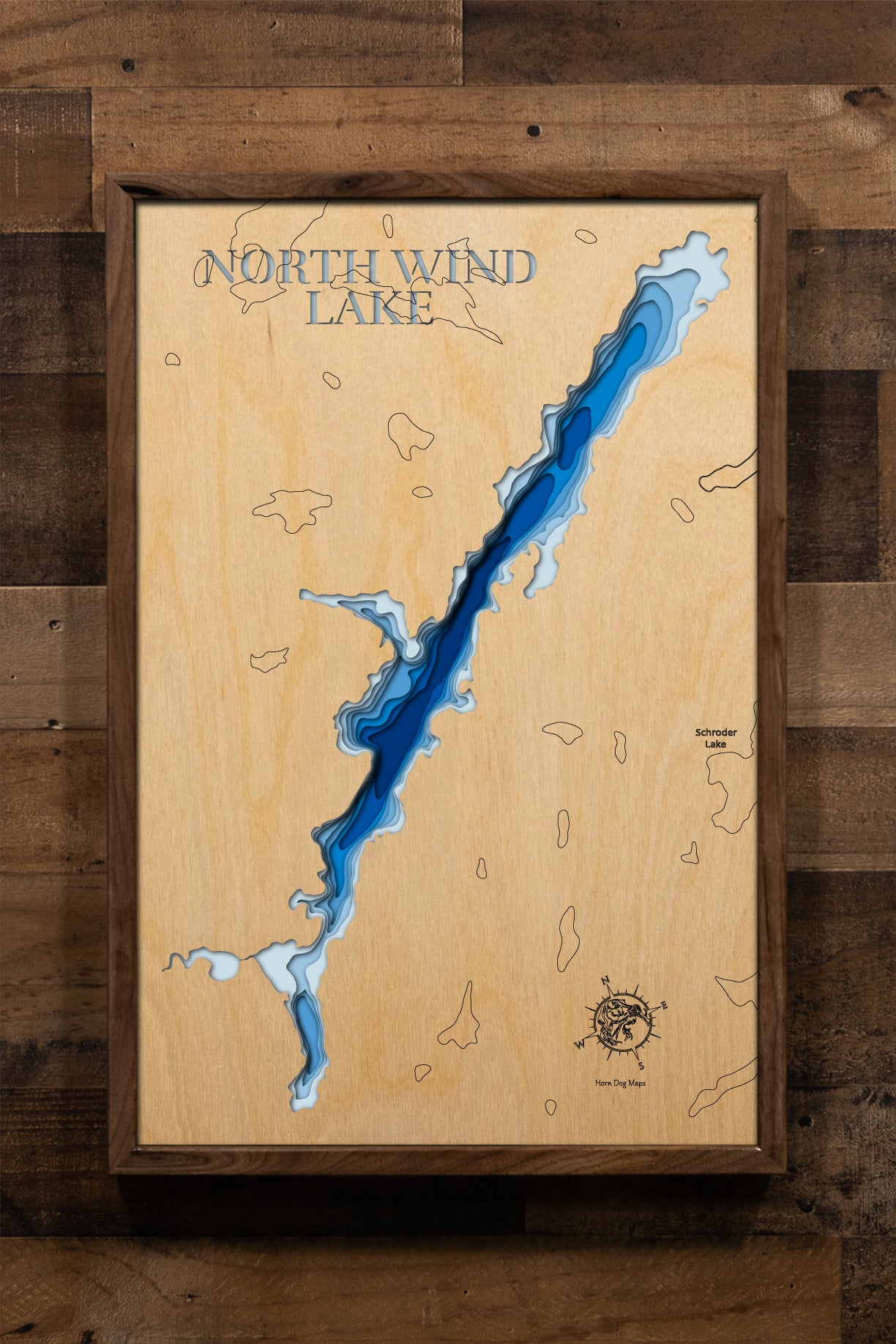 A magnificently detailed, laser-cut, multi-layered wooden topographical map of North Wind Lake in Thunder Bay District, Ontario, showcasing the lake's pristine wilderness setting with intricate shoreline winding through untouched boreal forest and detailed depth contours from shallow vegetated bays to deeper basins. The natural wood top layer frames the remote lake's natural character, while graduated blue layers create a stunning visual depth gradient across this premier Northwestern Ontario fishing destin
