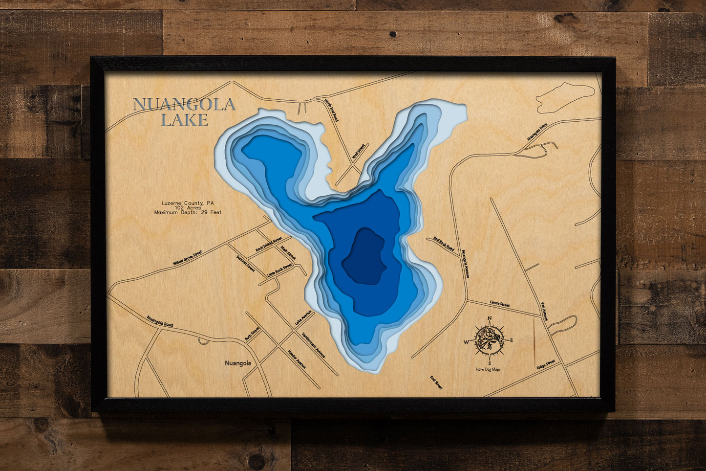 A precision laser-cut, multi-layered wooden map of Nuangola Lake in Luzerne County, Pennsylvania — a 102-acre heart-shaped lake nestled in a historic resort borough in the Wyoming Valley highlands. The natural wood top layer captures the lake's distinctive triangular shoreline in fine detail, while a light-to-dark blue gradient conveys its 29-foot depth. A handcrafted statement piece for any Pennsylvania lake home, Pocono-area cabin, or outdoor enthusiast's wall.