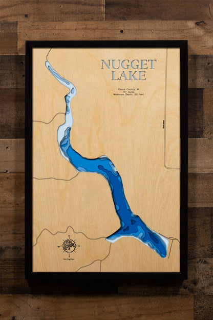 A precision laser-cut, multi-layered wooden map of Nugget Lake in Pierce County, Wisconsin — a 117-acre Plum Creek flowage near Plum City set within 752 acres of semi-wilderness at Nugget Lake County Park. The natural wood top layer captures the lake's elongated shoreline in fine detail, while a light-to-dark blue gradient conveys its 50-foot depth. A handcrafted statement piece for any Wisconsin lake cabin, home, or outdoor enthusiast's wall.