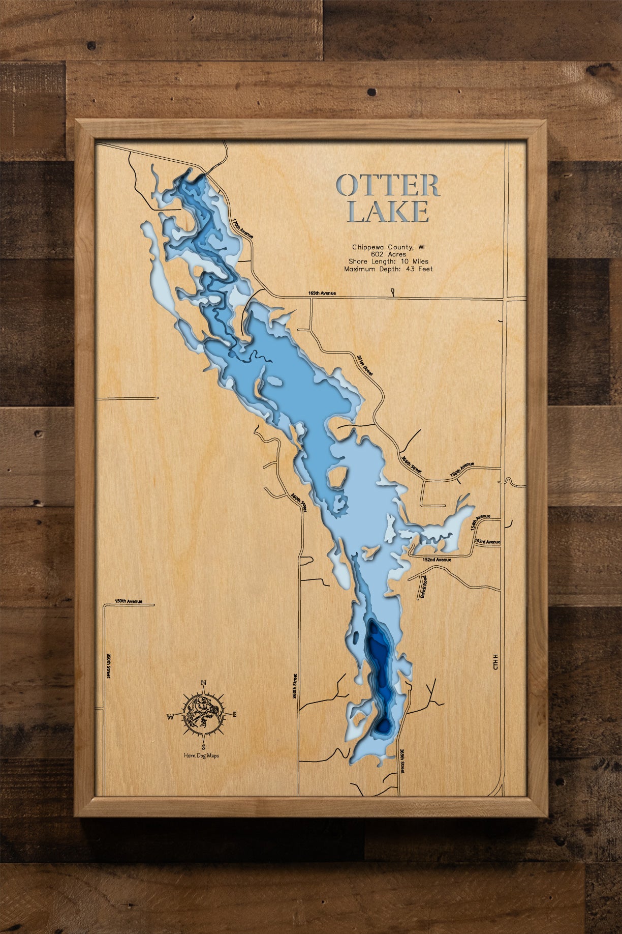 A meticulously detailed, laser-cut, multi-layered wooden topographical map of Otter Lake in Chippewa County, Wisconsin, showcasing the 602-acre reservoir created in 1969 with depth contours from the 11-foot average to the 43-foot maximum depth. The natural wood top layer frames approximately 10 miles of shoreline including the historic dam, Otter Lake County Park with 22 campsites, four public boat launches, and two aeration systems, while graduated blue layers create a striking visual depth gradient across