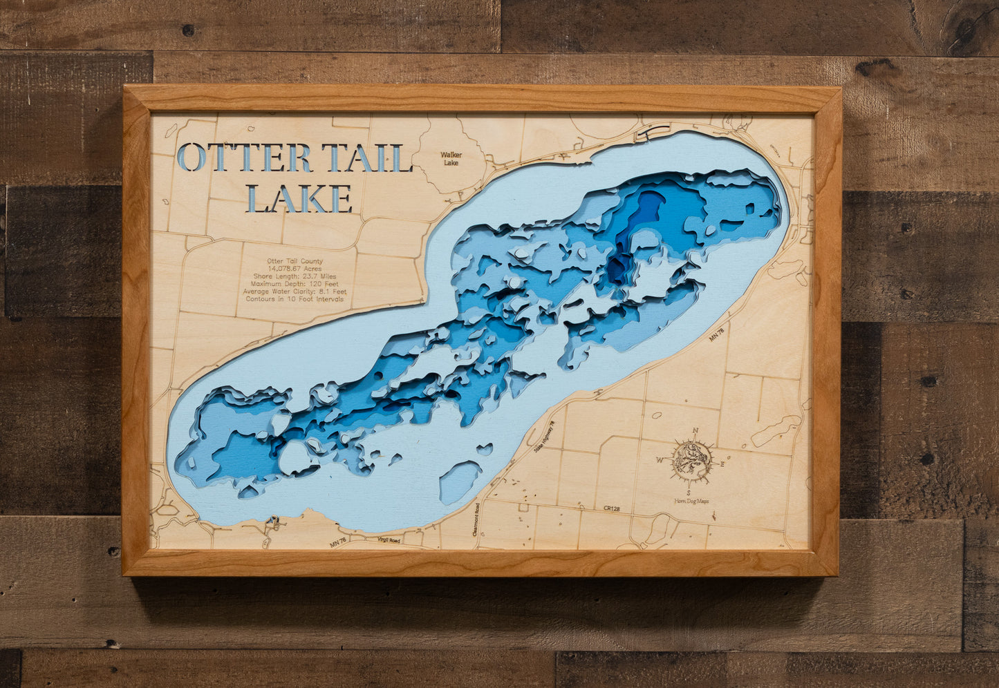 A laser-cut, layered wooden map of Otter Tail Lake in Otter Tail County, Minnesota. The distinct shape of this large natural lake, with its 23.7-mile shoreline, is clearly visible within the forested landscape of west-central Minnesota. The varying depths of the lake, reaching a remarkable maximum of 120 feet, are represented by different layers of wood, illustrating its impressive underwater topography.