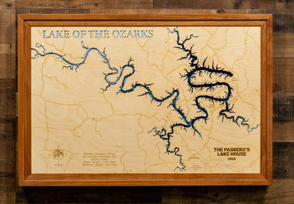 A framed wooden topographic map of Lake of the Ozarks, featuring blue river and lake features on a light wood background, enclosed in a medium brown wood frame and mounted on a dark wood wall.