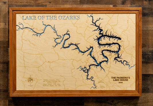 A framed wooden topographic map of Lake of the Ozarks, featuring blue river and lake features on a light wood background, enclosed in a medium brown wood frame and mounted on a dark wood wall.
