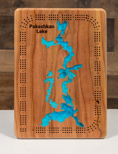 A magnificently detailed, laser-cut, multi-layered wooden topographical map of Pakashkan Lake in Thunder Bay District, Ontario, showcasing the sprawling 13,141-acre surface with three distinct basins and intricate 60 miles of wilderness shoreline. The natural wood top layer frames rocky reefs, protected bays, and the Grew-Weaver Canoe Route connections, while graduated blue layers create a stunning visual gradient from shallow river inlets to the 70-foot maximum depth.