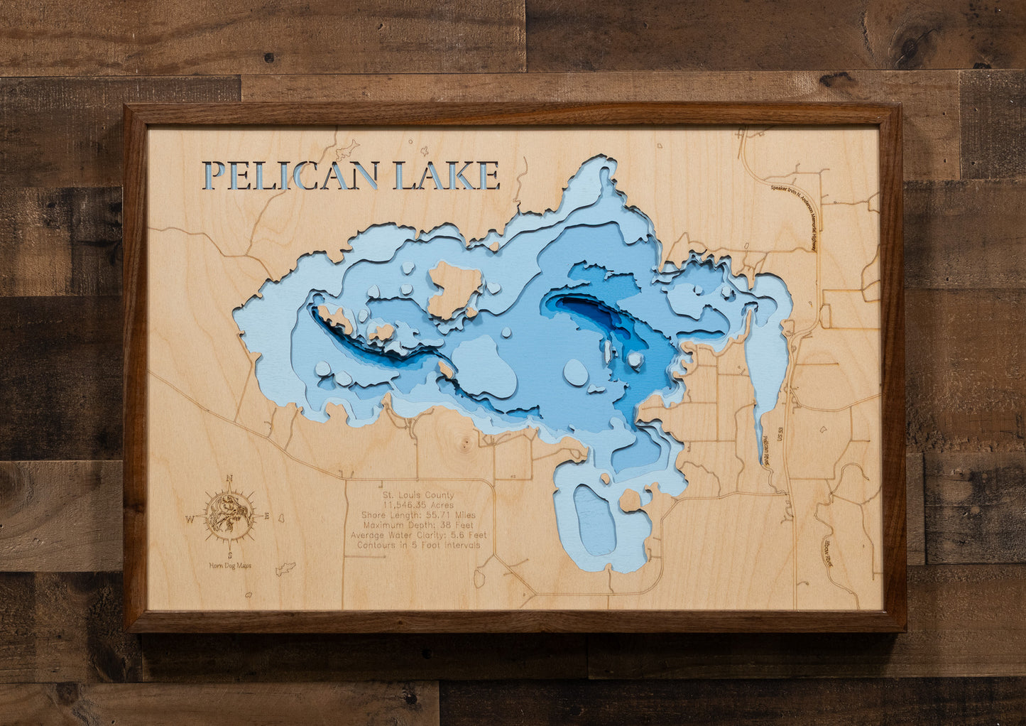 A laser-cut, layered wooden map of Pelican Lake in St. Louis County, Minnesota. The distinct shape of this large lake, with its 55.71-mile shoreline and numerous islands, is clearly visible within the forested landscape of northern Minnesota near the town of Orr. The varying depths of the lake, reaching a maximum of 40 feet, are represented by different layers of wood, illustrating its impressive underwater topography.