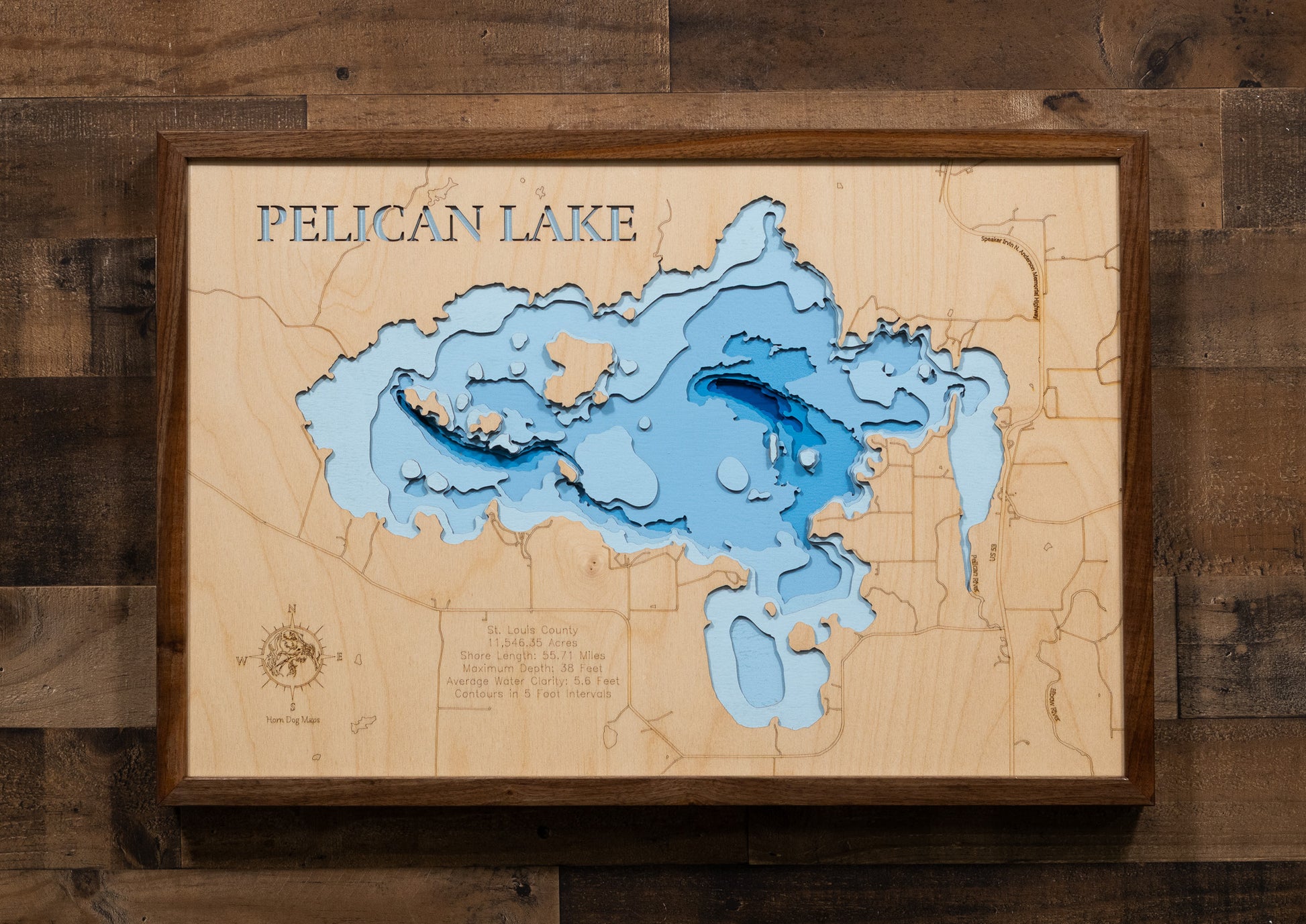 A laser-cut, layered wooden map of Pelican Lake in St. Louis County, Minnesota. The distinct shape of this large lake, with its 55.71-mile shoreline and numerous islands, is clearly visible within the forested landscape of northern Minnesota near the town of Orr. The varying depths of the lake, reaching a maximum of 40 feet, are represented by different layers of wood, illustrating its impressive underwater topography.