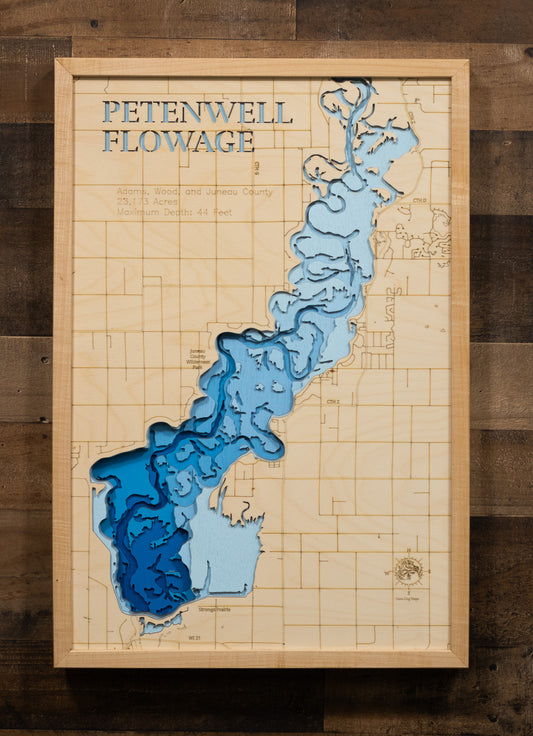 A laser-cut, layered wooden map of Petenwell Flowage in Adams, Juneau, and Wood counties, Wisconsin. The distinct shape of this vast artificial lake on the Wisconsin River, with its 101.07-mile shoreline, is clearly visible within the forested landscape of central Wisconsin. The varying depths of the flowage, reaching a maximum of 44 feet, are represented by different layers of wood, illustrating its underwater topography.
