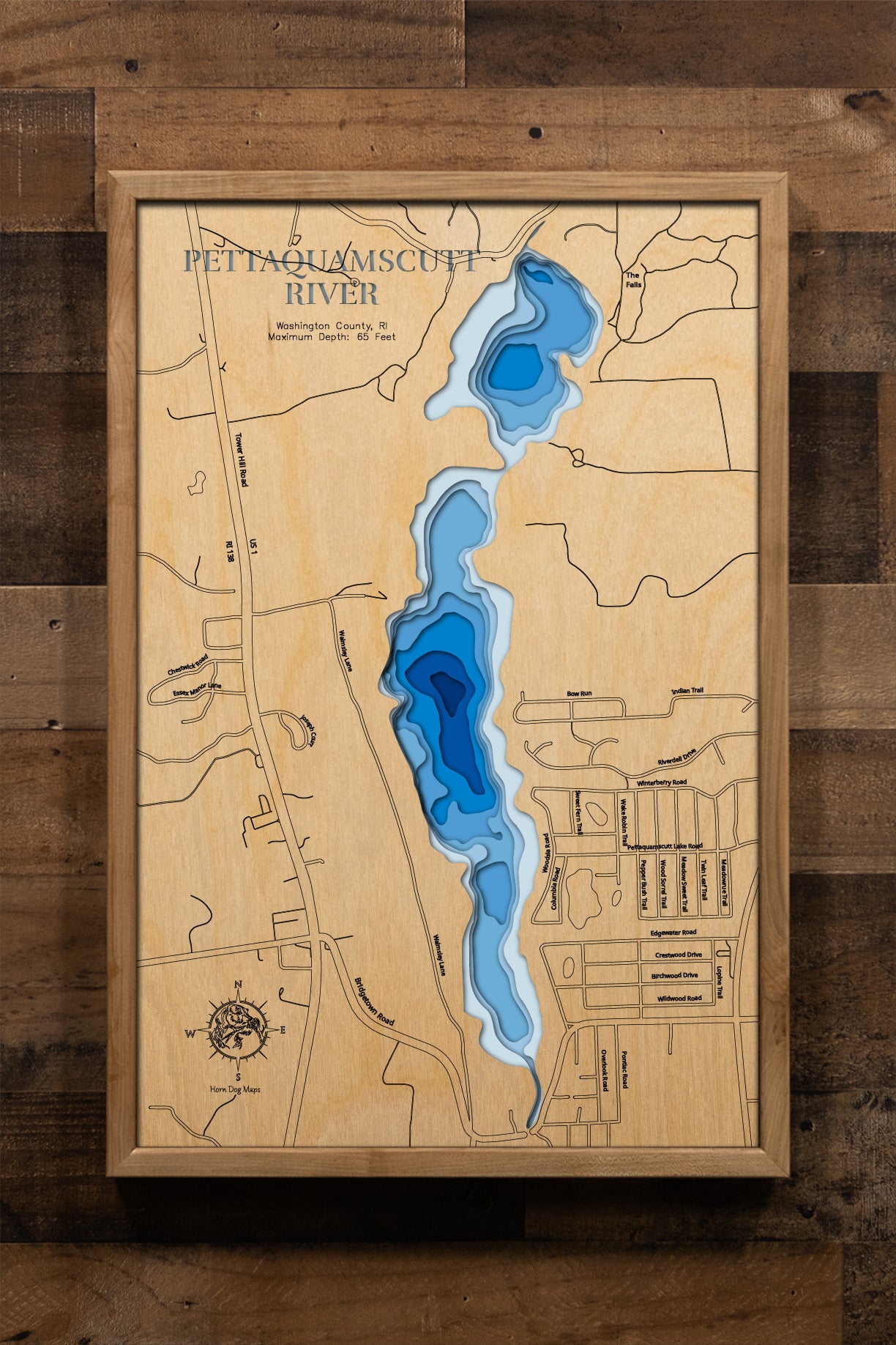 A meticulously detailed, laser-cut, multi-layered wooden map of the Pettaquamscutt River in Washington County, Rhode Island, showcasing the six-mile tidal estuary's winding course through North Kingstown, South Kingstown, and Narragansett. The topographic design features natural wood layers and graduated blue water depths from shallow marshes to the remarkable 65-foot Lower Pond basin.