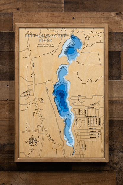 A meticulously detailed, laser-cut, multi-layered wooden map of the Pettaquamscutt River in Washington County, Rhode Island, showcasing the six-mile tidal estuary's winding course through North Kingstown, South Kingstown, and Narragansett. The topographic design features natural wood layers and graduated blue water depths from shallow marshes to the remarkable 65-foot Lower Pond basin.