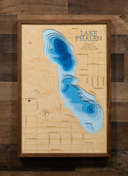 A laser-cut, layered wooden map of Lake Phalen in Ramsey County, Minnesota. The shape of the lake, with its 3.02-mile shoreline, is visible within the suburban landscape of Ramsey County. The varying depths of the lake, reaching a maximum of 91 feet and detailed by 10-foot contour intervals, are represented by different layers of wood, illustrating its underwater topography.