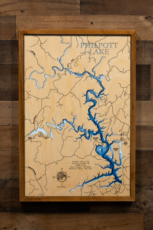 A magnificently detailed, laser-cut, multi-layered wooden topographical map of Philpott Lake in Franklin, Henry, and Patrick Counties, Virginia, showcasing the pristine 2,880-acre reservoir with 100 miles of undeveloped wilderness shoreline surrounded by nearly 20,000 acres of protected land. The natural wood top layer frames the Smith River arm, dramatic cliffs, and Philpott Dam, while graduated blue layers create a stunning visual gradient from shallow upper reaches to the astounding 180-foot maximum dept