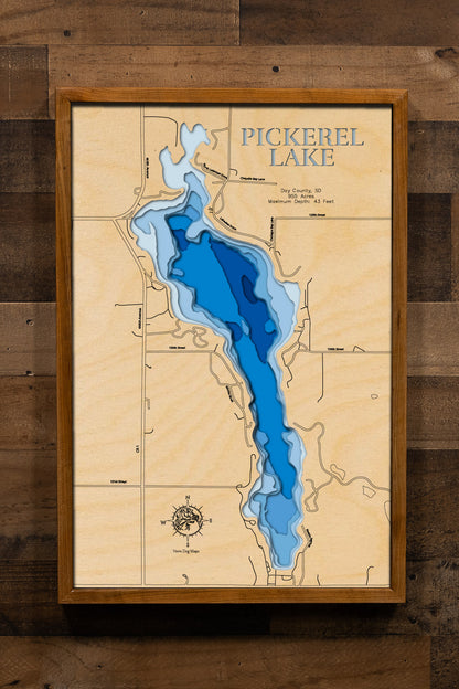 A beautifully detailed, laser-cut wooden topographic map of Pickerel Lake in Day County, South Dakota, featuring layered depth contours illustrating the impressive 43-foot maximum depth making it one of the state's deepest natural lakes, the 955-acre spring-fed basin with clear glacial waters, the locations of East and West Campgrounds with their boat launches and beaches, surrounding Ponderosa pine forests, and the distinctive glacial landscape of northeastern South Dakota's Prairie Pothole Region.