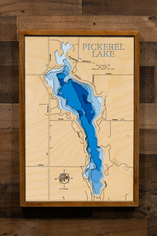 A beautifully detailed, laser-cut wooden topographic map of Pickerel Lake in Day County, South Dakota, featuring layered depth contours illustrating the impressive 43-foot maximum depth making it one of the state's deepest natural lakes, the 955-acre spring-fed basin with clear glacial waters, the locations of East and West Campgrounds with their boat launches and beaches, surrounding Ponderosa pine forests, and the distinctive glacial landscape of northeastern South Dakota's Prairie Pothole Region.