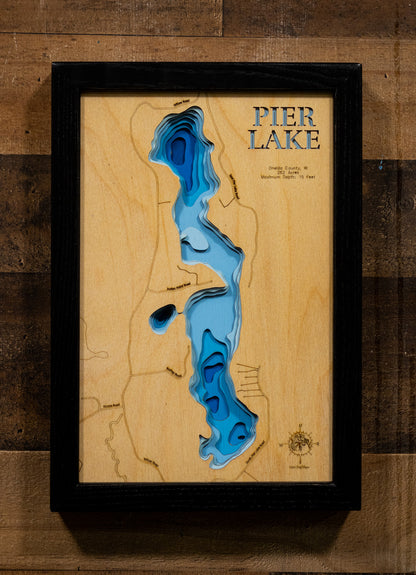 A precision laser-cut, multi-layered wooden map of Pier Lake in Oneida County, Wisconsin, a 262-acre warmwater lake near Minocqua holding Bass, Pike, Walleye, and Panfish. The natural wood top layer captures the lake's natural shoreline in fine detail, while a light-to-dark blue gradient conveys its shallow, productive character. A handcrafted statement piece for any Wisconsin Northwoods cabin, lake home, or outdoor enthusiast's wall.