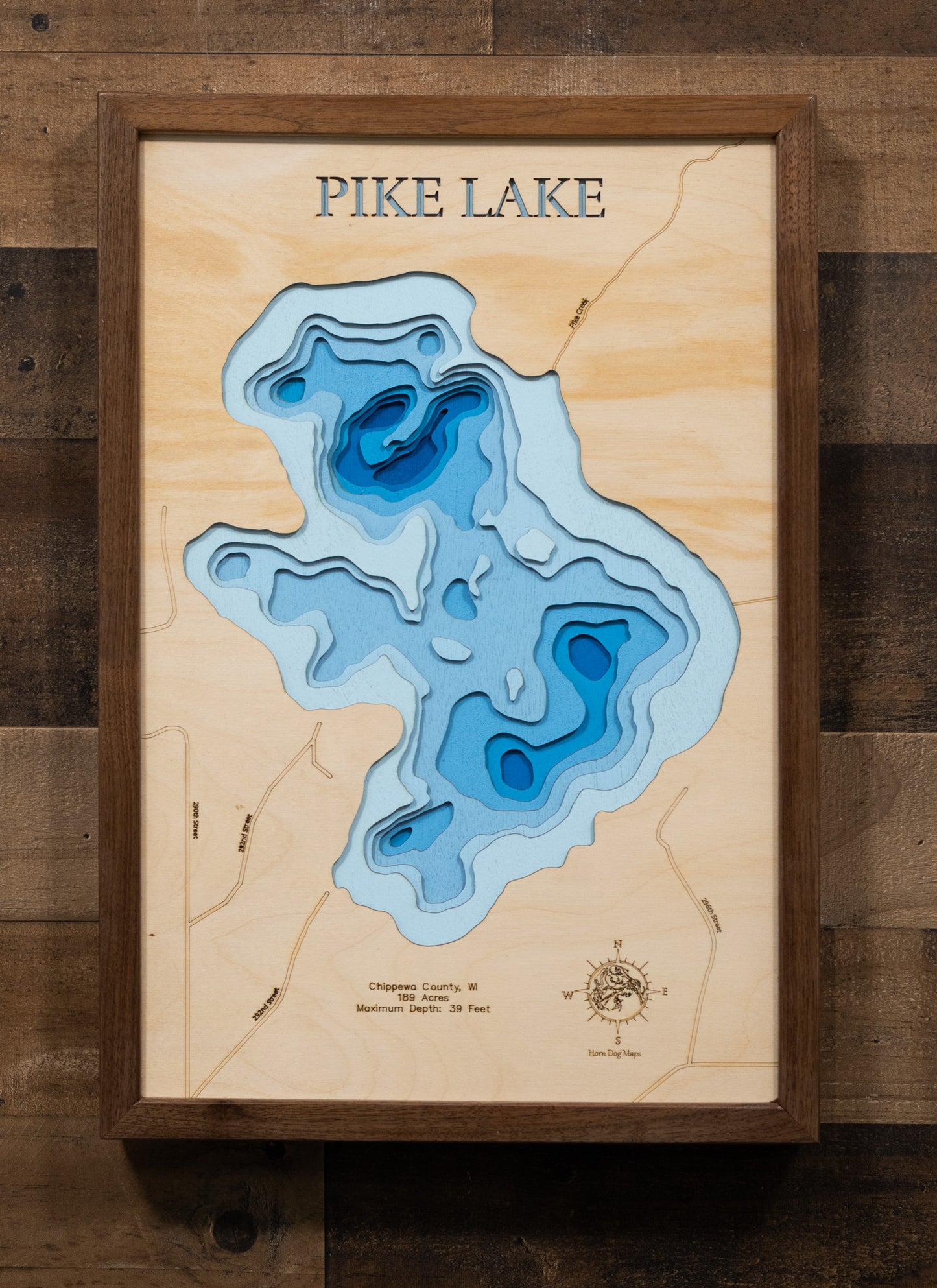 A highly detailed, laser-cut, and multi-layered wooden map of Pike Lake, a natural lake in Chippewa County, Wisconsin. The map shows the lake's distinct shape and its 2.15-mile shoreline. The varying depths of the lake, reaching a maximum of 35 feet, are represented by different layers of wood.