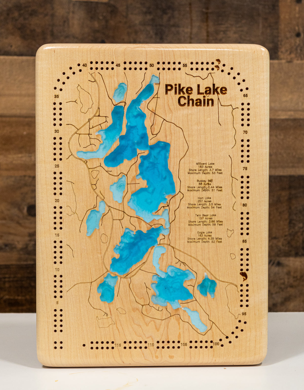 A cribbage board game titled "Pike Lake Chain" featuring a printed map of blue lakes on a light natural wood background, photographed against a dark wood backdrop.