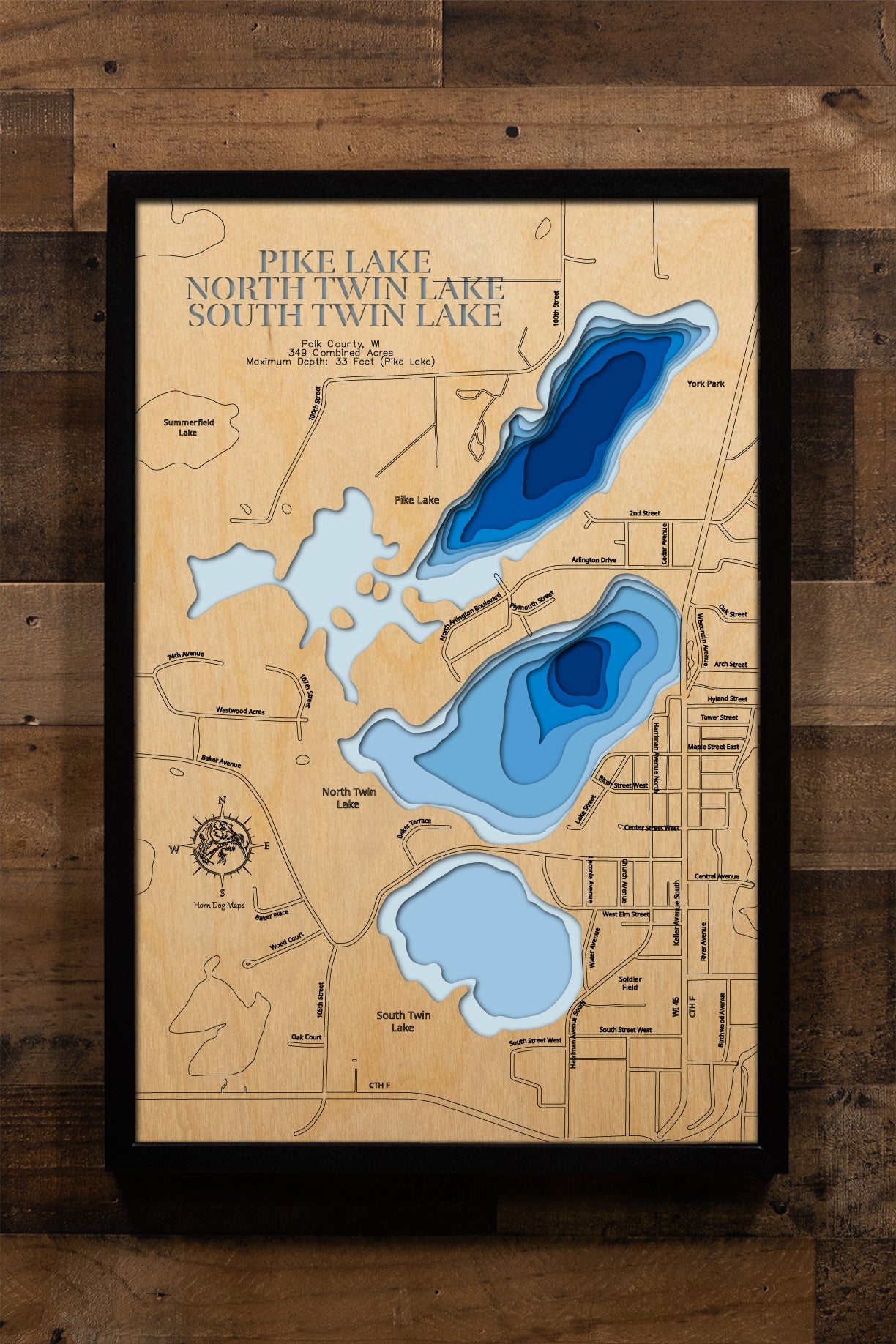 A precision laser-cut, multi-layered wooden map of the Pike Lake Chain — Pike, North Twin, and South Twin Lakes — in Polk County, Wisconsin. The natural wood top layer traces the interconnected shorelines of all three lakes in fine detail, while a light-to-dark blue gradient highlights their varying depths. A distinctive, rustic statement piece crafted for cabin walls, lake homes, or any Wisconsin lake-inspired living space.