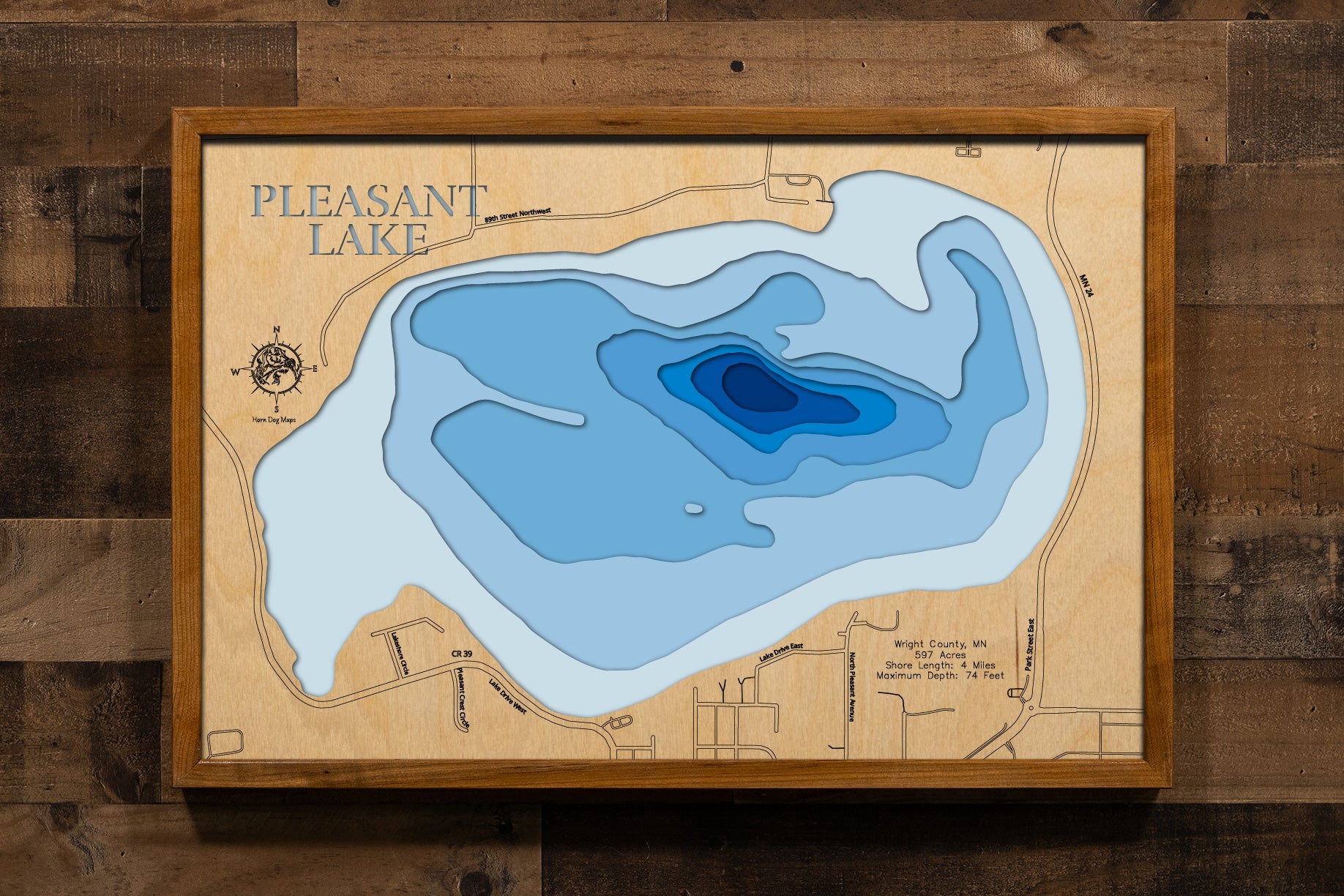A detailed, laser-cut, multi-layered wooden map of Pleasant Lake in Wright County, Minnesota, showcasing the 597-acre lake with 4 miles of shoreline within Clearwater/Pleasant Regional Park near Annandale. The topographic design features natural wood layers highlighting the two public accesses and county park amenities, with graduated blue water layers illustrating depths to the impressive 74-foot maximum.