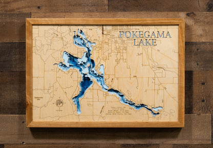 A laser-cut, layered wooden map of Pokegama Lake in Itasca County, Minnesota. The distinct, complex shape of this large natural lake, with its 58.26-mile shoreline, is clearly visible within the forested landscape of northern Minnesota. The varying depths of the lake, reaching a remarkable maximum of 110 feet, are represented by different layers of wood, illustrating its impressive underwater topography.