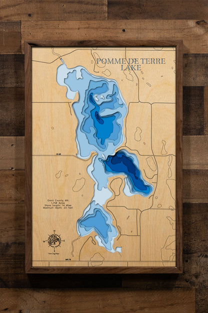 A precision laser-cut, multi-layered wooden map of Pomme de Terre Lake in Grant County, Minnesota, a 1,758-acre shallow prairie lake on the Pomme de Terre River between Elbow Lake and Ashby. The natural wood top layer captures 14 miles of undeveloped shoreline in fine detail, while a light-to-dark blue gradient conveys the lake's broad, flatwater character. A handcrafted statement piece for any Minnesota lake home, cabin, or outdoor enthusiast's wall.
