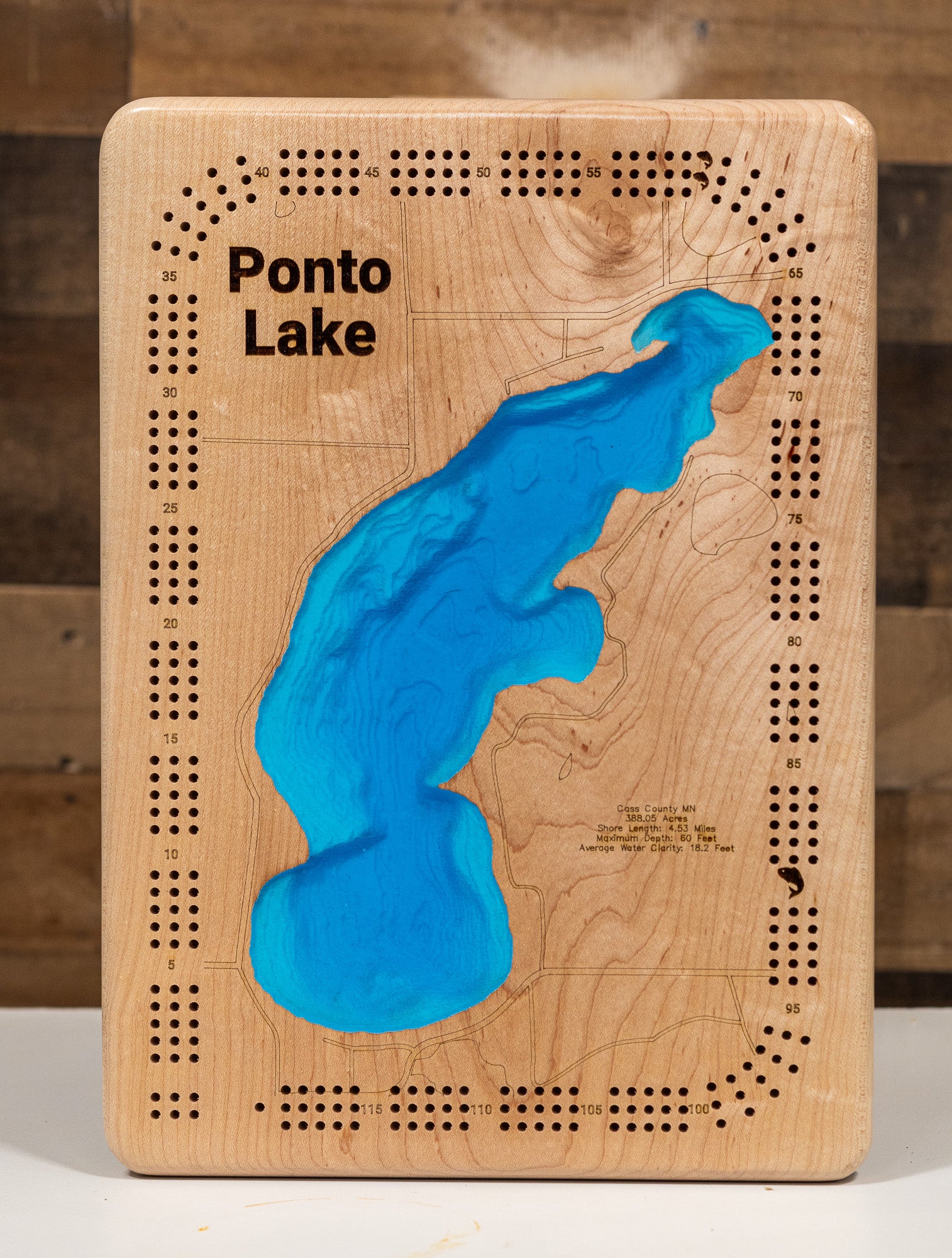 A cribbage board featuring an engraved topographic map of Ponto Lake with a raised bright blue lake design in the center. The board has laser-cut holes around the edges and the words 'Ponto Lake' printed near the top left.