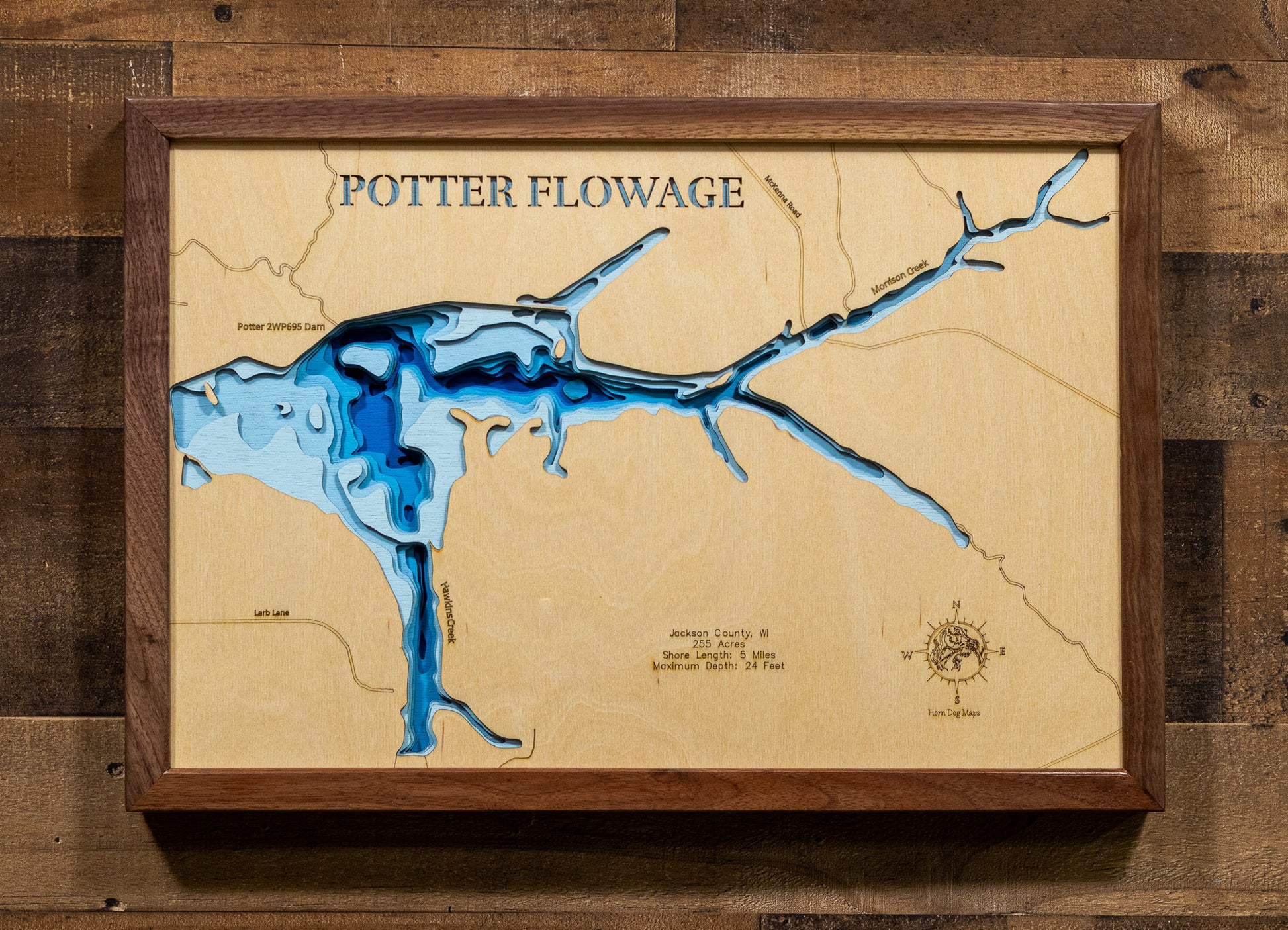 A meticulously detailed, laser-cut, multi-layered wooden topographical map of Potter Flowage in Jackson County, Wisconsin, showcasing the 255-acre impoundment's distinctive T-shape with McKenna and Morrison Creek inlets, numerous bays along approximately five miles of pine-lined shoreline, and extensive lily pad beds. The natural wood top layer frames the dark-water flowage with depth contours from the 7-foot average to the 24-foot maximum near the dam, while graduated blue layers create a gentle visual dep