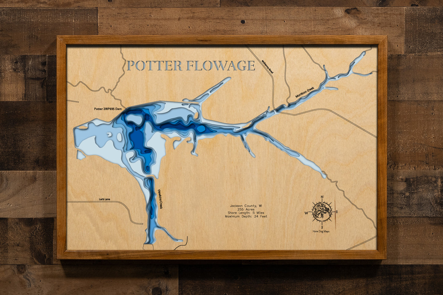 A meticulously detailed, laser-cut, multi-layered wooden topographical map of Potter Flowage in Jackson County, Wisconsin, showcasing the 255-acre impoundment's distinctive T-shape with McKenna and Morrison Creek inlets, numerous bays along approximately five miles of pine-lined shoreline, and extensive lily pad beds. The natural wood top layer frames the dark-water flowage with depth contours from the 7-foot average to the 24-foot maximum near the dam, while graduated blue layers create a gentle visual dep