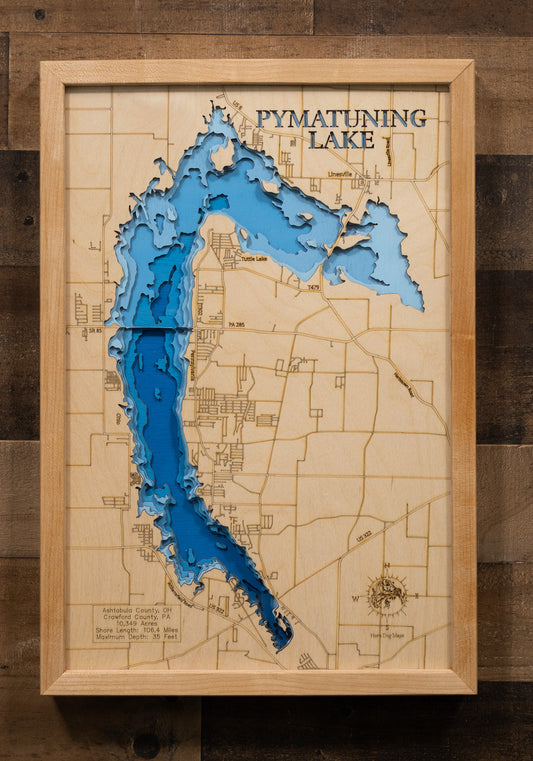 A highly detailed, 3D laser-cut wooden map of Pymatuning Reservoir in Ashtabula County, Ohio. The multi-layered design uses different wood tones to illustrate the lake's bathymetric contours and depths. Etched details include the reservoir's name, county lines, the causeway, and nearby towns like Andover, creating a unique and intricate piece of art.
