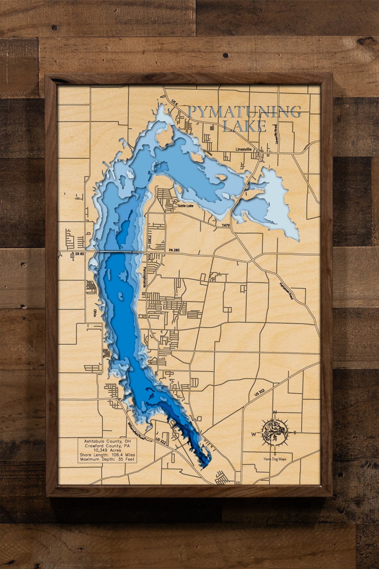 A highly detailed, 3D laser-cut wooden map of Pymatuning Reservoir in Ashtabula County, Ohio. The multi-layered design uses different wood tones to illustrate the lake's bathymetric contours and depths. Etched details include the reservoir's name, county lines, the causeway, and nearby towns like Andover, creating a unique and intricate piece of art.