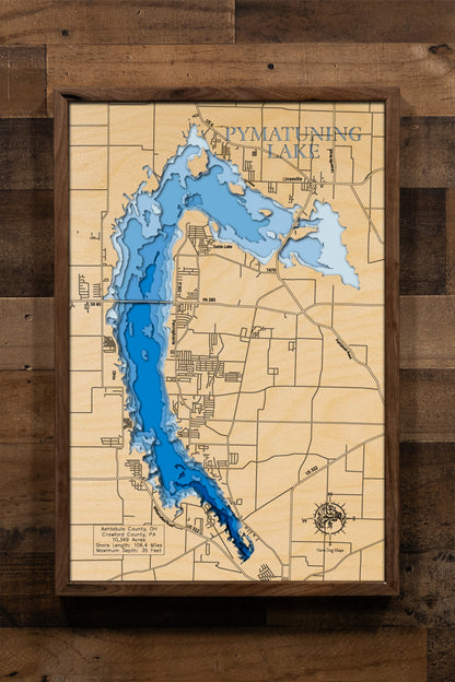 A highly detailed, 3D laser-cut wooden map of Pymatuning Reservoir in Ashtabula County, Ohio. The multi-layered design uses different wood tones to illustrate the lake's bathymetric contours and depths. Etched details include the reservoir's name, county lines, the causeway, and nearby towns like Andover, creating a unique and intricate piece of art.