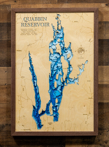 A laser-cut, layered wooden map of the Quabbin Reservoir, located in Hampshire, Franklin, and Worcester Counties, Massachusetts. The intricate and lengthy shoreline of this significant water body, with its many islands contributing to its unique shape, is clearly depicted in varying layers of wood to represent depth. The overall form of the reservoir within central Massachusetts is visually prominent.