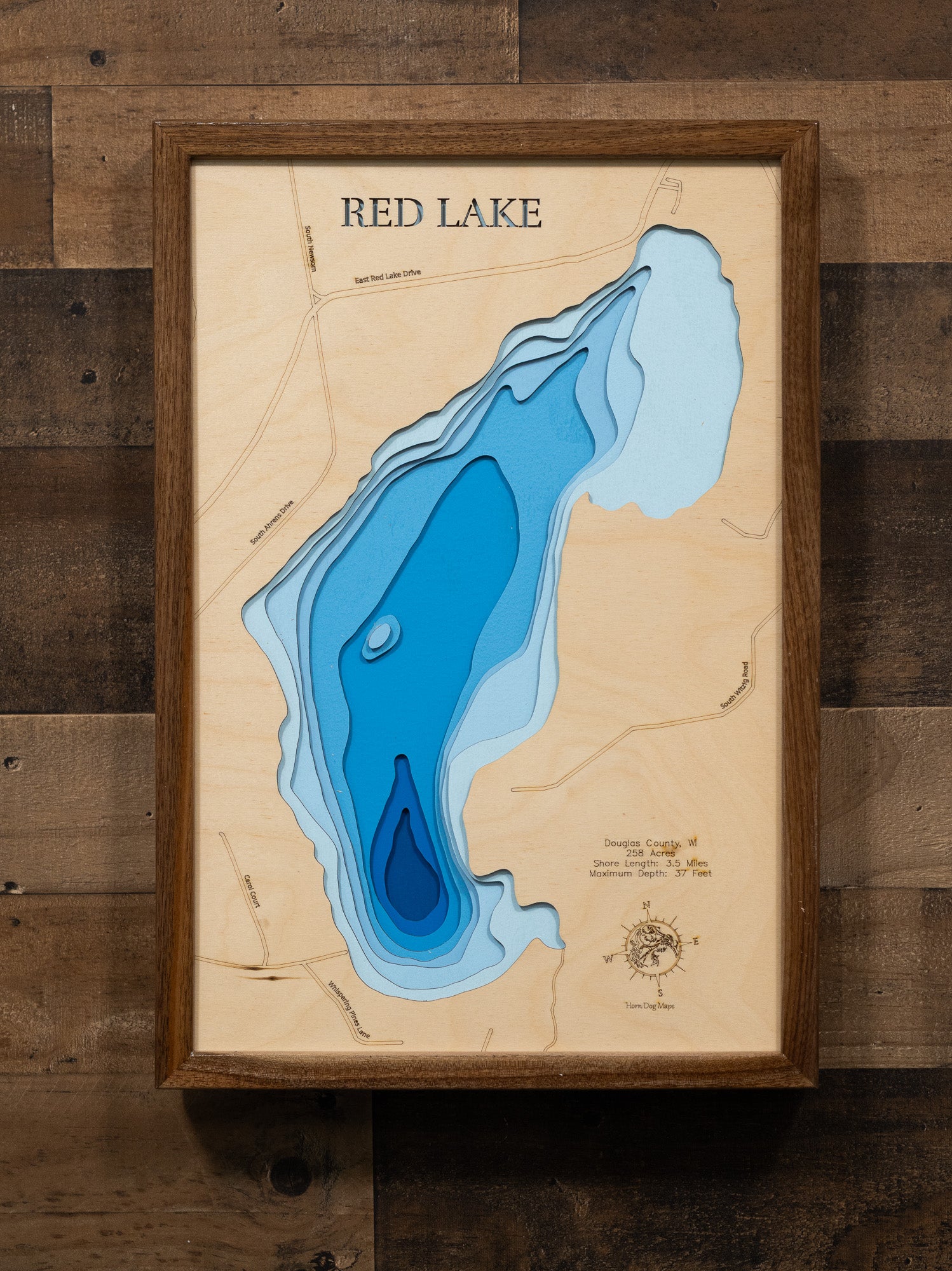 A laser-cut, layered wooden map of Red Lake in Douglas County, Wisconsin. The distinct shape of this natural lake, with its 3.5-mile shoreline, is clearly visible within the forested landscape of northern Wisconsin. The varying depths of the lake, reaching a maximum of 37 feet, are represented by different layers of wood, illustrating its impressive underwater topography.
