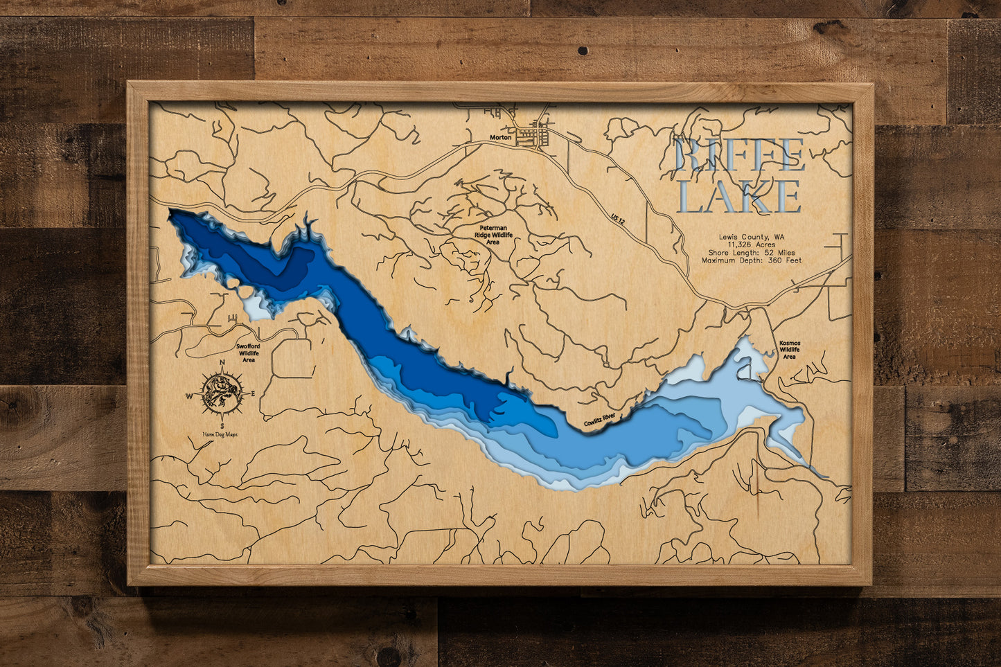 A precision laser-cut, multi-layered wooden map of Riffe Lake in Lewis County, Washington. The natural wood top layer captures 52 miles of dramatic mountain reservoir shoreline in fine detail, while a light-to-dark blue gradient highlights the lake's extraordinary depth — reaching 360 feet. A striking, rustic statement piece for any Pacific Northwest cabin, lake home, or outdoor enthusiast's space.
