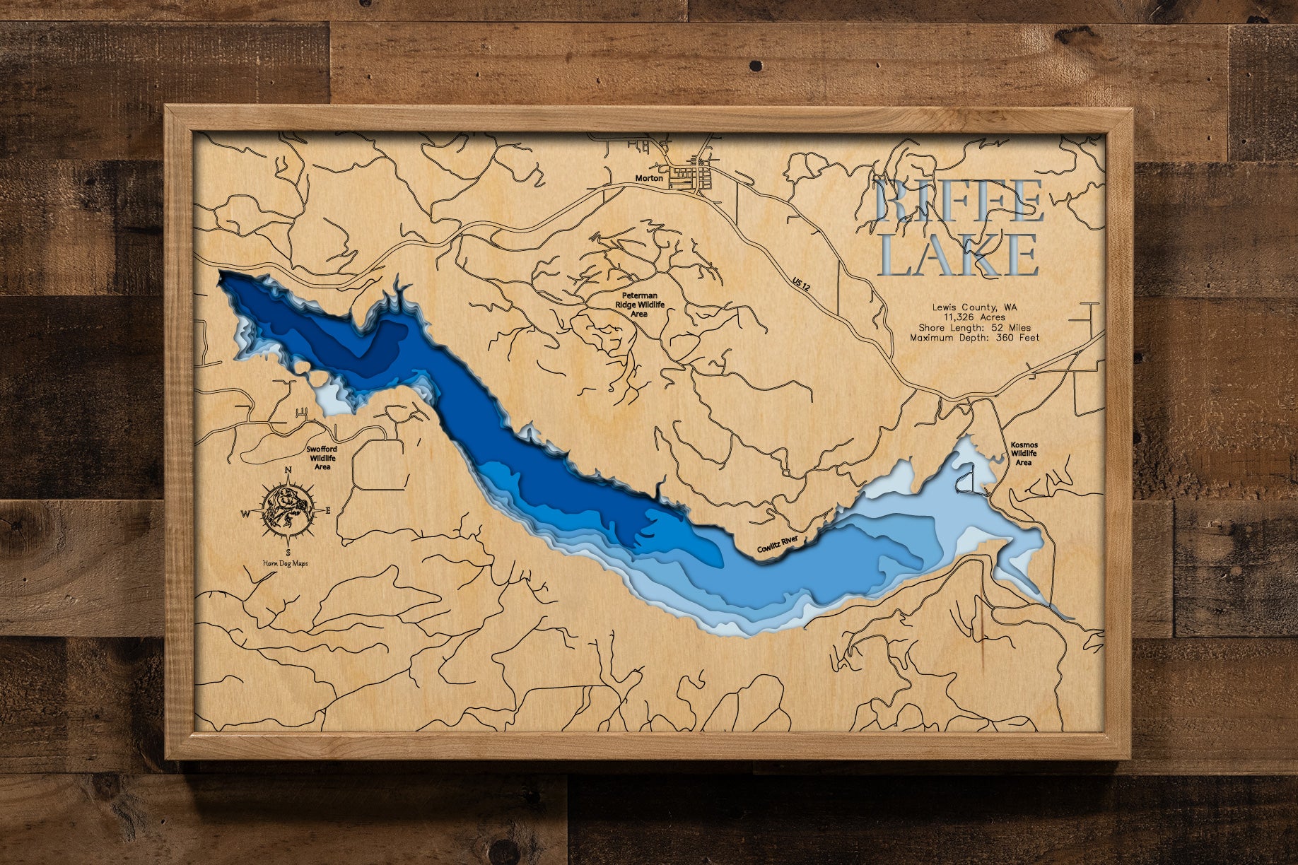 A precision laser-cut, multi-layered wooden map of Riffe Lake in Lewis County, Washington. The natural wood top layer captures 52 miles of dramatic mountain reservoir shoreline in fine detail, while a light-to-dark blue gradient highlights the lake's extraordinary depth — reaching 360 feet. A striking, rustic statement piece for any Pacific Northwest cabin, lake home, or outdoor enthusiast's space.