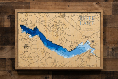 A precision laser-cut, multi-layered wooden map of Riffe Lake in Lewis County, Washington. The natural wood top layer captures 52 miles of dramatic mountain reservoir shoreline in fine detail, while a light-to-dark blue gradient highlights the lake's extraordinary depth — reaching 360 feet. A striking, rustic statement piece for any Pacific Northwest cabin, lake home, or outdoor enthusiast's space.