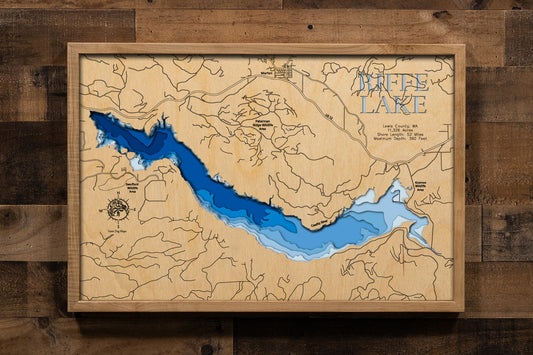 A precision laser-cut, multi-layered wooden map of Riffe Lake in Lewis County, Washington. The natural wood top layer captures 52 miles of dramatic mountain reservoir shoreline in fine detail, while a light-to-dark blue gradient highlights the lake's extraordinary depth — reaching 360 feet. A striking, rustic statement piece for any Pacific Northwest cabin, lake home, or outdoor enthusiast's space.