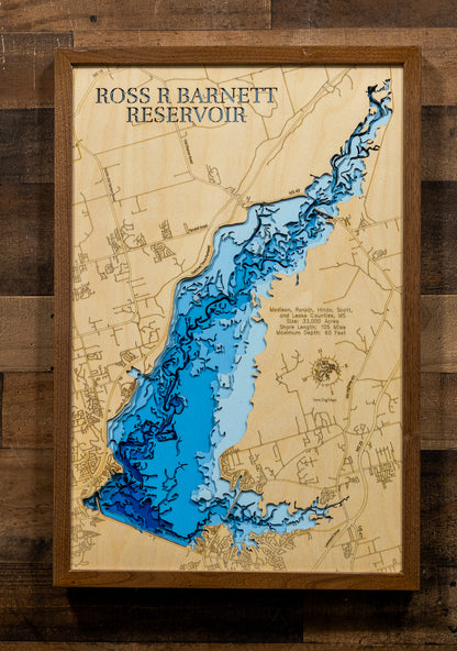 A framed wooden depth map of Ross R Barnett Reservoir, featuring layered blue and light blue water levels on a light wood background, mounted on a dark wood plank wall.