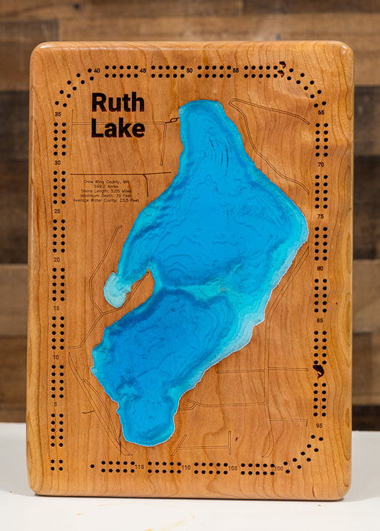 A cribbage board featuring a 3D resin map of 'Ruth Lake' in bright blue, set against a warm honey-toned wood grain background with pre-drilled holes around the border.