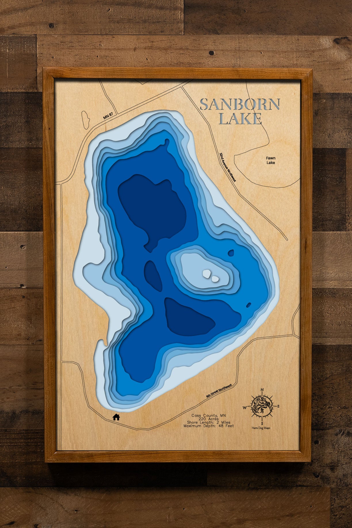 A precision laser-cut, multi-layered wooden map of Sanborn Lake in Cass County, Minnesota, a clear water lake east of Backus near Hackensack in the heart of Paul Bunyan Country. The natural wood top layer captures 2 miles of shoreline in fine detail, while a light-to-dark blue gradient conveys the lake's 48-foot depth. A handcrafted statement piece for any Minnesota lake cabin, home, or outdoor enthusiast's wall.