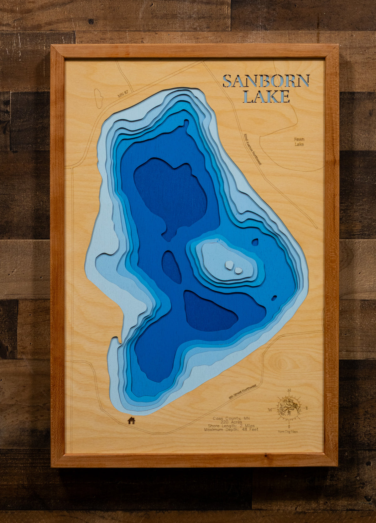 A precision laser-cut, multi-layered wooden map of Sanborn Lake in Cass County, Minnesota, a clear water lake east of Backus near Hackensack in the heart of Paul Bunyan Country. The natural wood top layer captures 2 miles of shoreline in fine detail, while a light-to-dark blue gradient conveys the lake's 48-foot depth. A handcrafted statement piece for any Minnesota lake cabin, home, or outdoor enthusiast's wall.