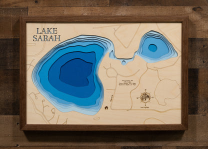 A laser-cut, layered wooden map of Lake Sarah in Polk County, Minnesota. The distinct shape of this natural lake, with its 5.27-mile shoreline, is clearly visible within the landscape of northwestern Minnesota near Erskine. The varying depths of the lake, reaching a maximum of 27 feet, are represented by different layers of wood, illustrating its impressive underwater topography.
