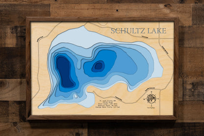 A laser-cut, layered wooden map of Schultz Lake in St. Louis County, Minnesota. The shape of the lake is visible within the northeastern Minnesota landscape. The varying depths of the lake, reaching a maximum of 48 feet, are represented by different layers of wood.
