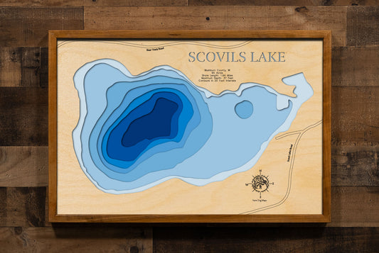 A laser-cut, layered wooden map of Scovils Lake in Washburn County, Wisconsin. The distinct shape of this natural lake, with its 1.64-mile shoreline, is clearly visible within the forested landscape of northern Wisconsin. The varying depths of the lake, reaching a maximum of 37 feet and detailed by 25-foot contour intervals, are represented by different layers of wood, illustrating its impressive underwater topography.