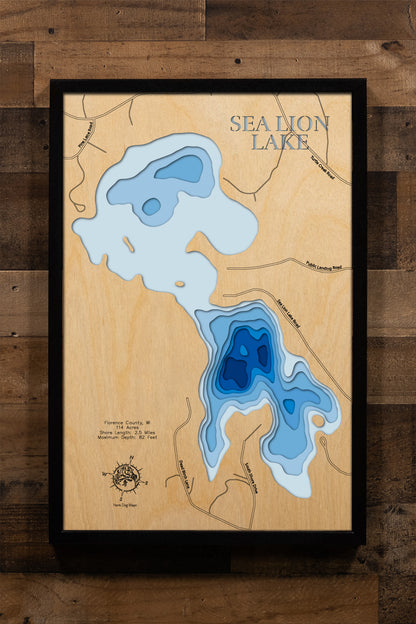 A meticulously detailed, laser-cut, multi-layered wooden topographical map of Sea Lion Lake in Florence County, Wisconsin, showcasing the lake's 114-acre surface with intricate depth contours illustrating the dramatic transition from the 16-foot average depth to the impressive 82-foot maximum depth. The natural wood top layer frames 2.5 miles of precisely rendered shoreline, while graduated blue layers create a striking visual depth gradient.