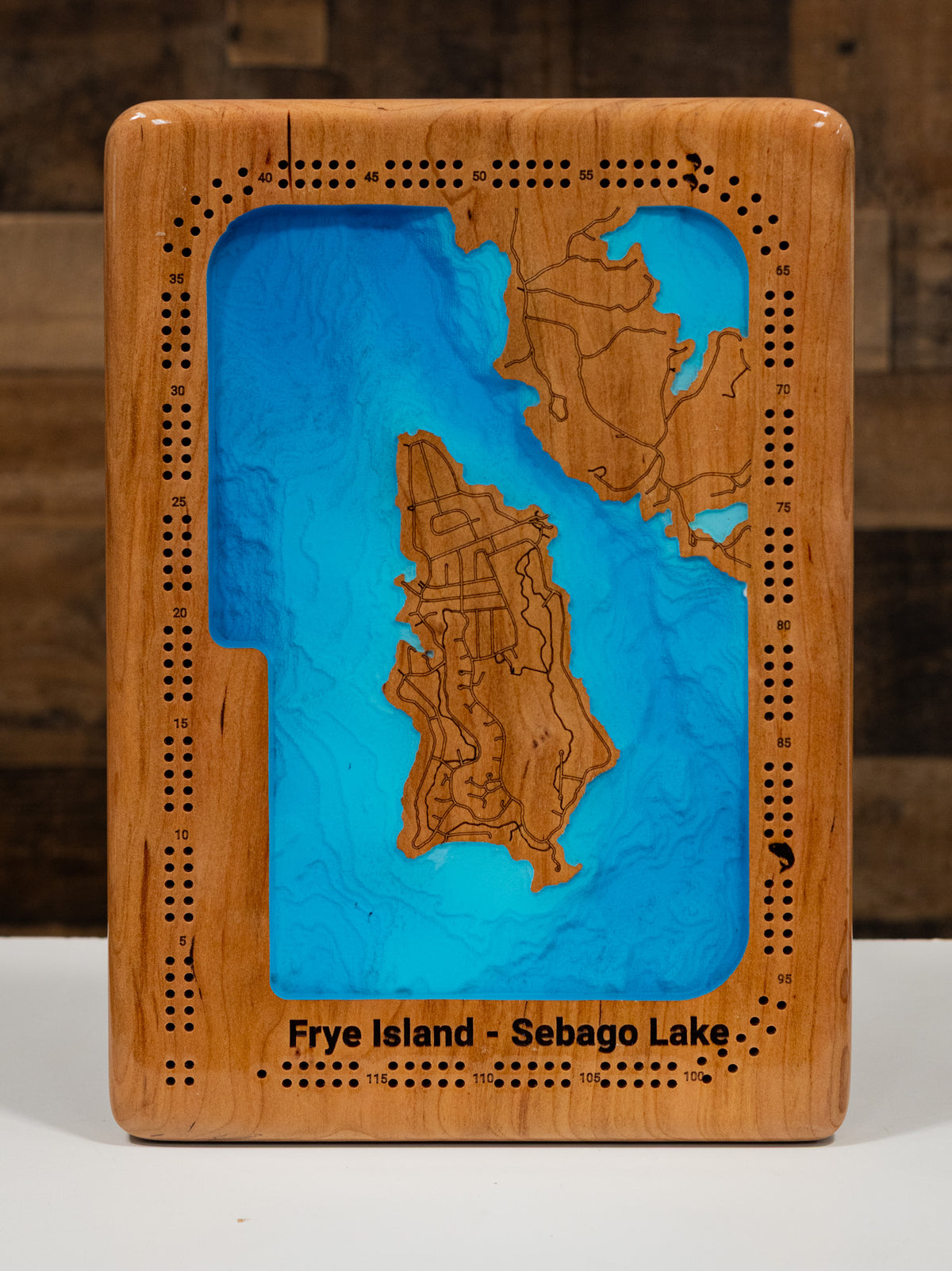 A square wooden plaque featuring a 3D map of Frye Island and Sebago Lake, with a natural wood border, laser-engraved details, and a white surface underneath.