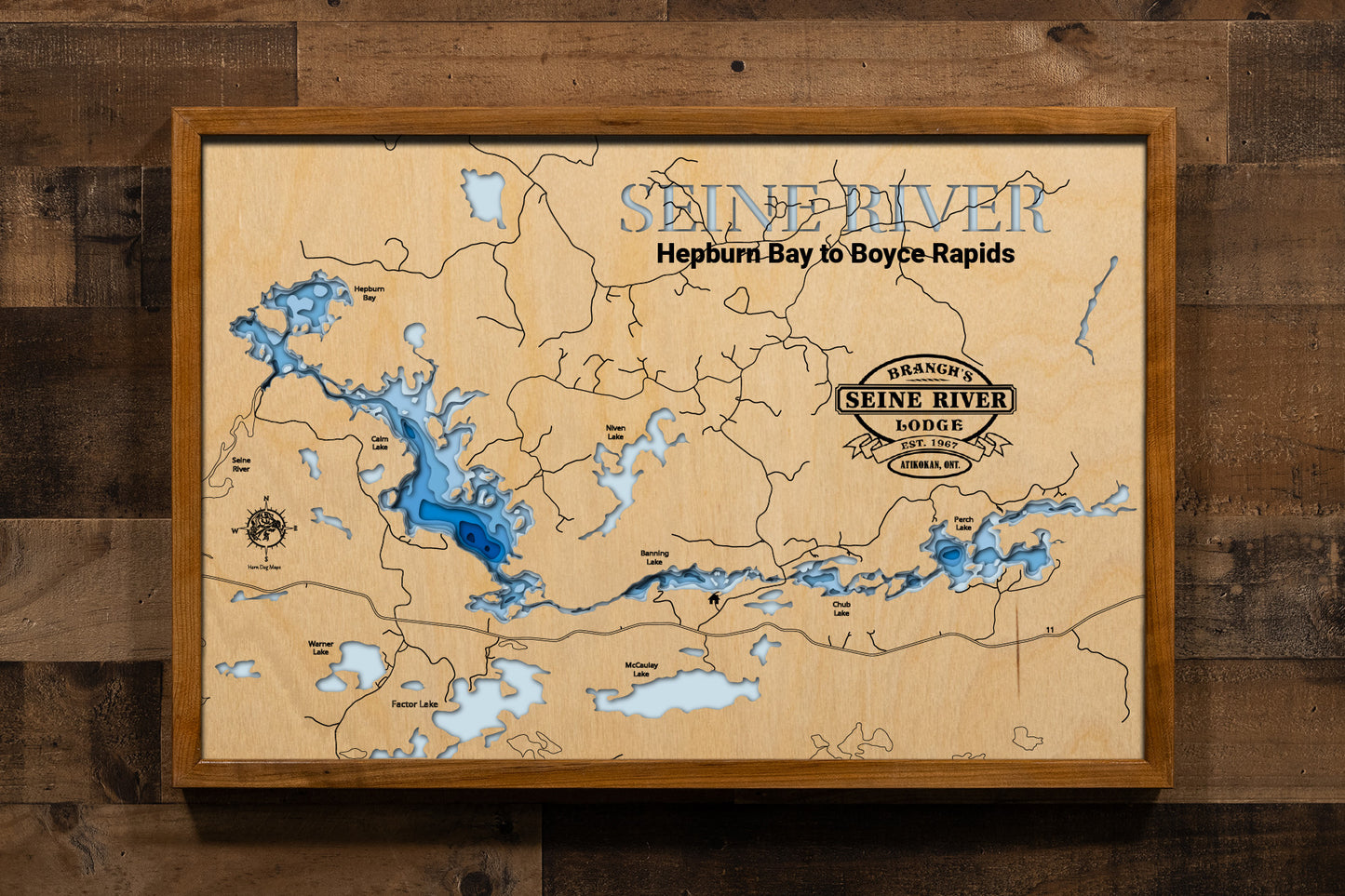 A precision laser-cut, multi-layered wooden map of the Seine River Chain of Lakes from Calm Lake to Perch Lake in Ontario's Rainy River District. The natural wood top layer traces over 30 miles of connected river channels, narrows, and lake basins in striking detail, while a light-to-dark blue gradient conveys depths exceeding 200 feet in Calm Lake. A handcrafted statement piece for any Ontario fishing camp, wilderness cabin, or Atikokan-area enthusiast's wall.